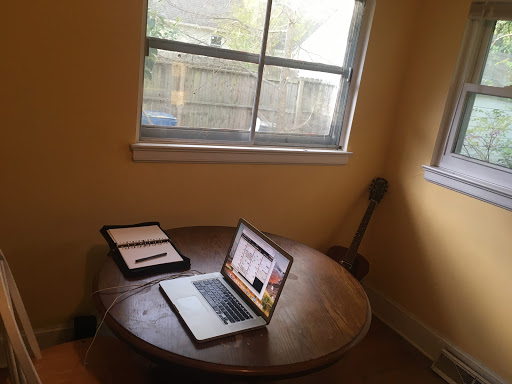 A photo of the same brown table in the same yellow room featuring only a laptop and notebook.