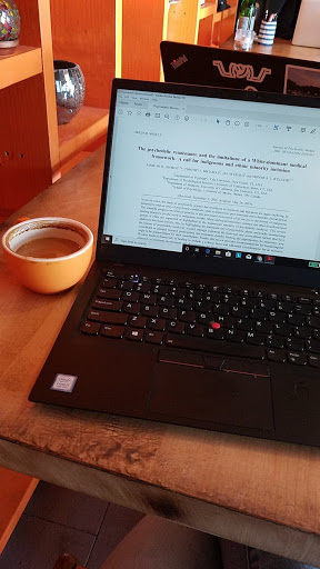 On the left is coffee in an orange mug on a table. On the right is a black laptop with an article pulled up on the screen.