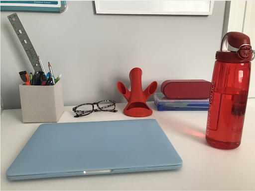 Author's desk is arranged neatly with a laptop, water bottle, glasses, and pencil case.