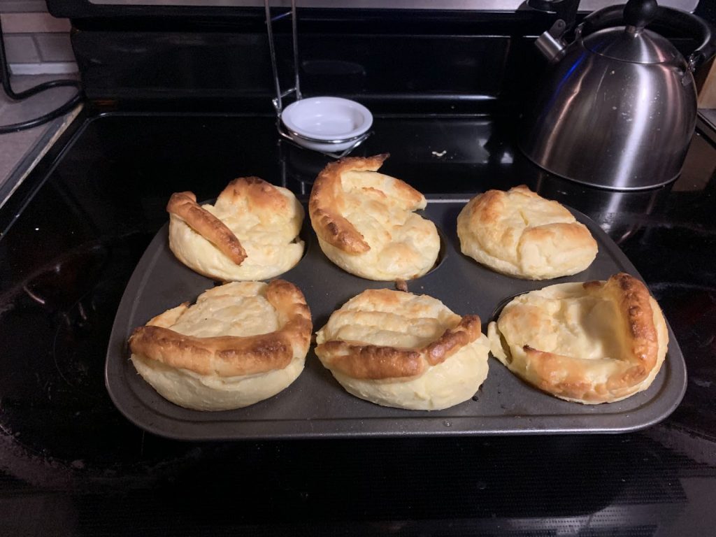 Six Yorkshire puddings in a muffin tin on a black stove next to a tea kettle