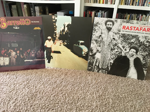 Three album covers featuring Caribbean music artists in front of a book shelf.