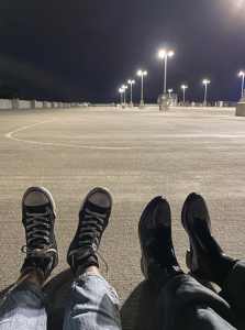 My friend and I staring at our feet while we sit in a large parking lot illuminated by lampposts. 