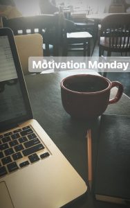 A cup of coffee next to a laptop in a local coffee shop with "Motivation Monday" written in text. 